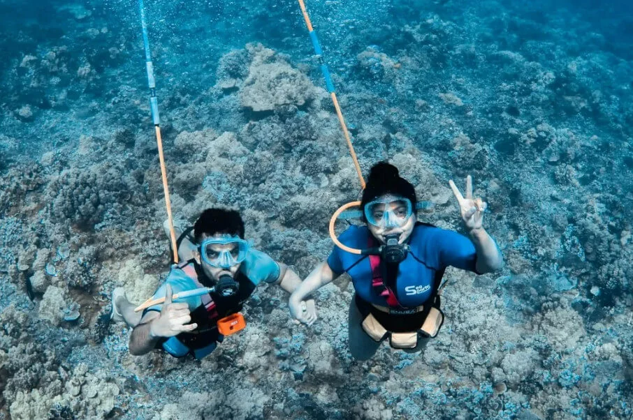 duas pessoas com roupa de mergulho posam para uma foto no fundo do mar
